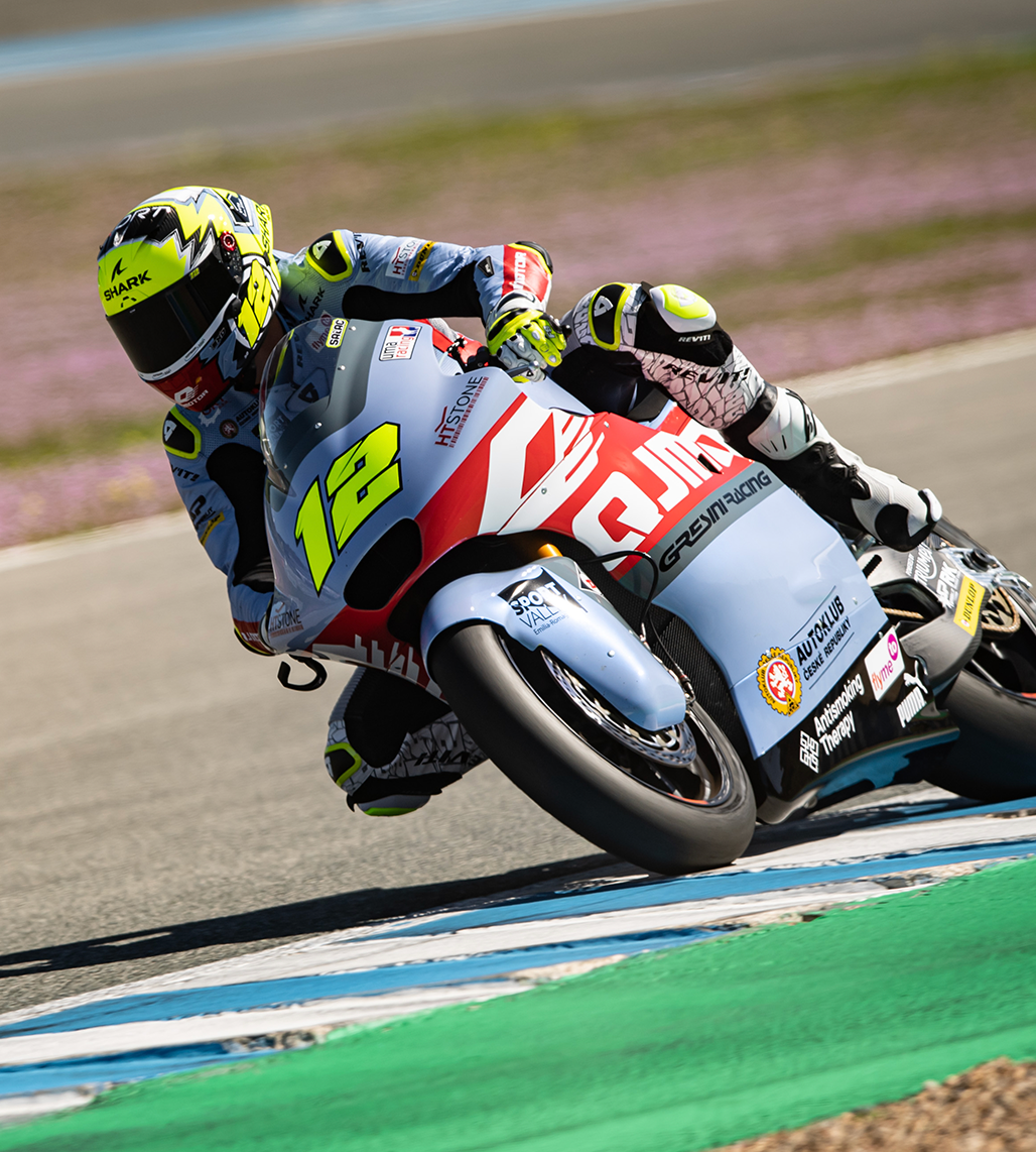 Un motociclista con il numero 12 su una moto azzurra e rossa si inclina in curva su un circuito asfaltato.