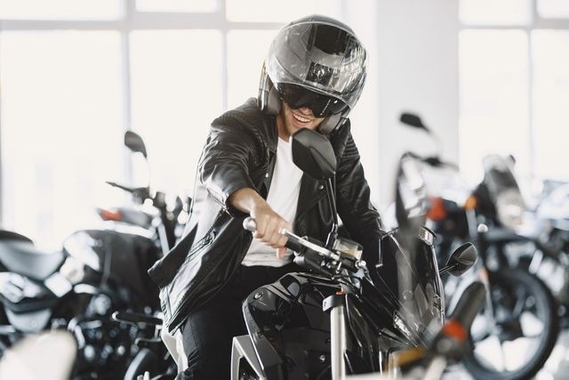 In uno showroom, una persona con indosso una giacca di pelle nera e un casco da motociclista è seduta