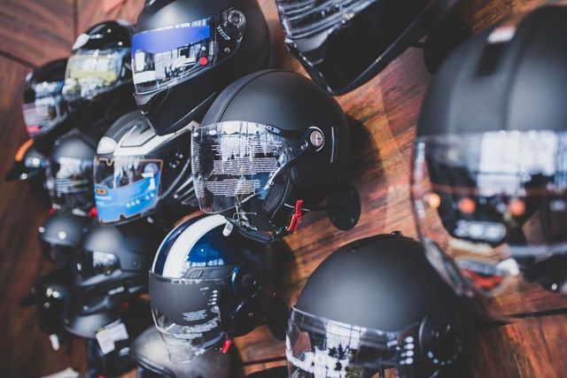 Una parete espositiva con diversi caschi da motociclista neri opachi, dotati di visiere trasparenti e colorate.