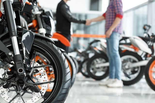 Due persone si stringono la mano in una concessionaria di motociclette, con un primo piano della ruota