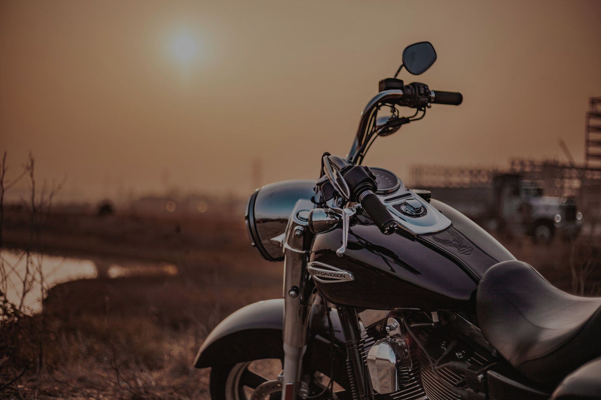 Primo piano di una motocicletta nera parcheggiata in un campo al tramonto, con una morbida luce dorata