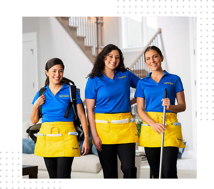 Three smiling cleaners in blue shirts and yellow aprons standing in a bright home interior.