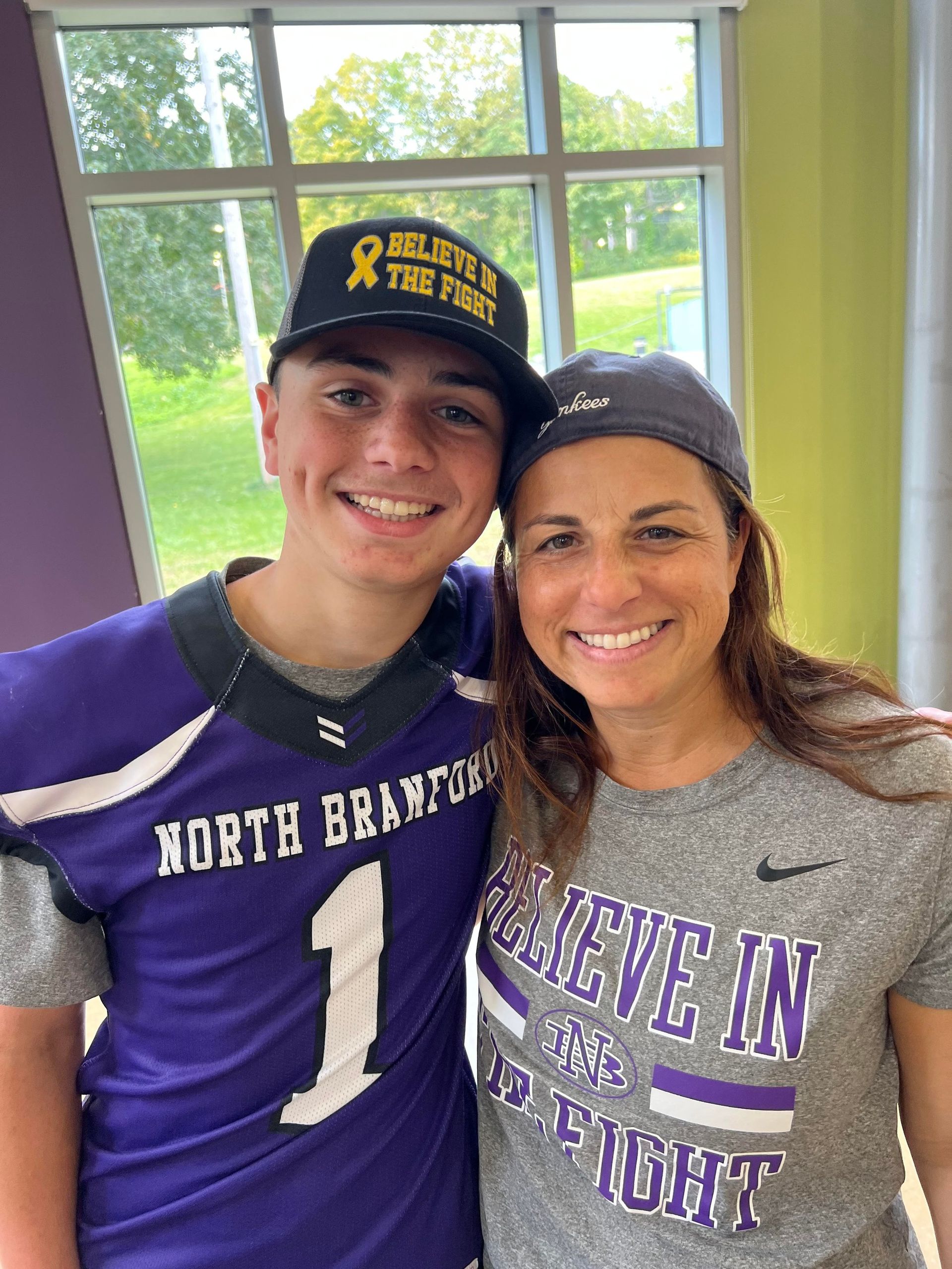 A man and a woman are posing for a picture . the man is wearing a purple football jersey.