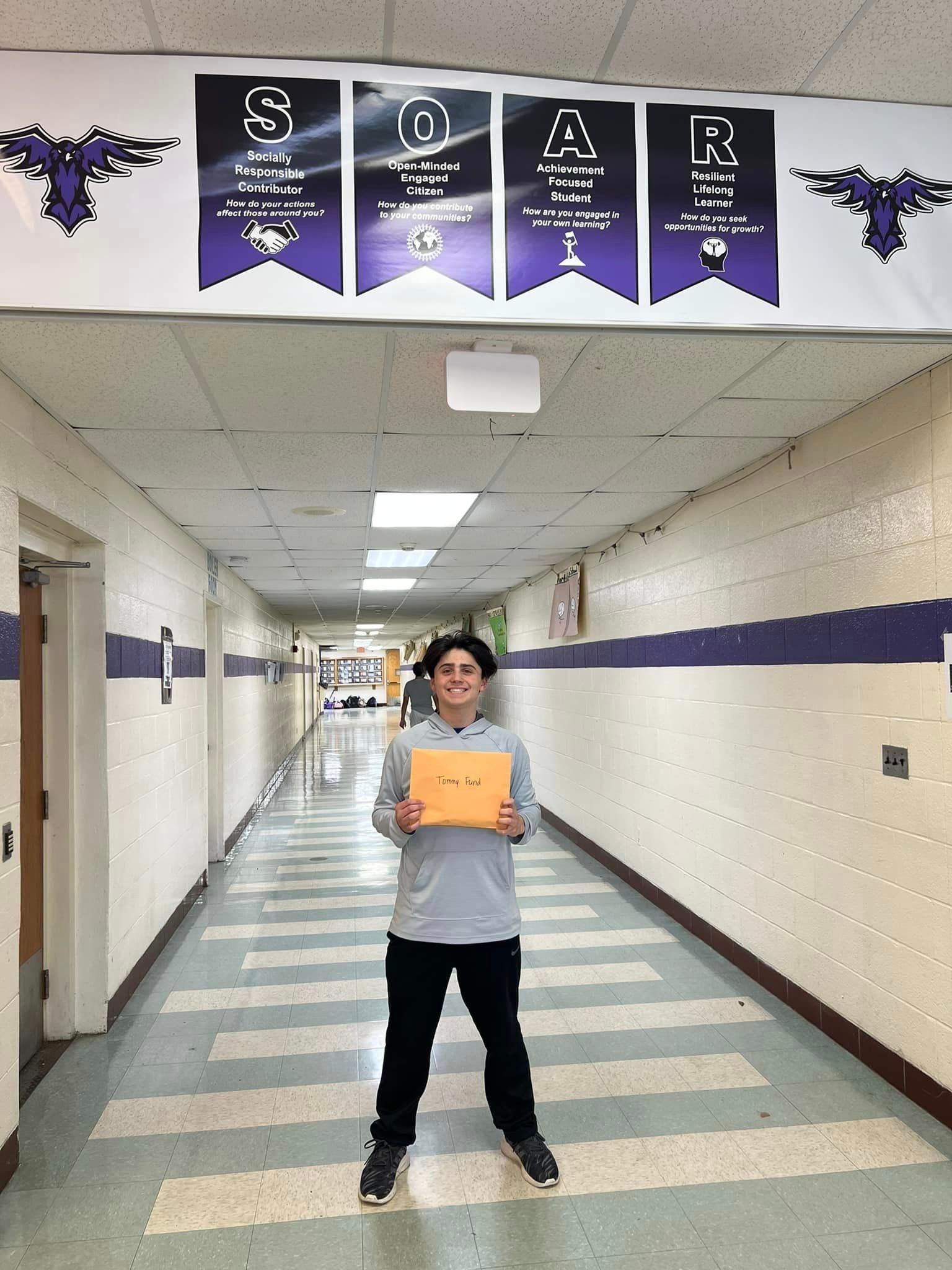 A young man is standing in a hallway holding an envelope
