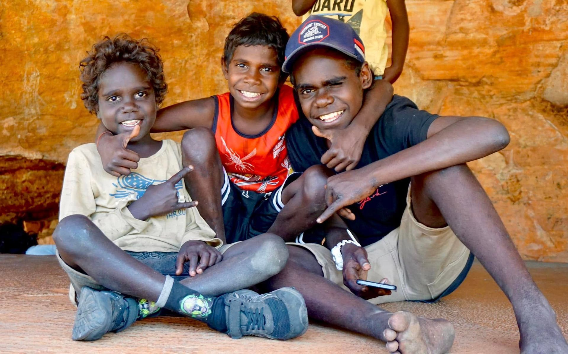 Three smiling Indigenous Australian children in casual clothes.