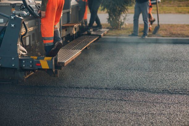 Road construction workers operating asphalt paving machine on freshly laid blacktop surface outdoors