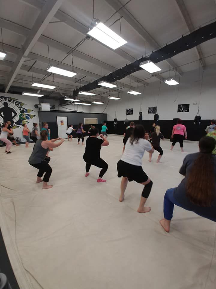 A group of people are squatting on a mat in a gym.