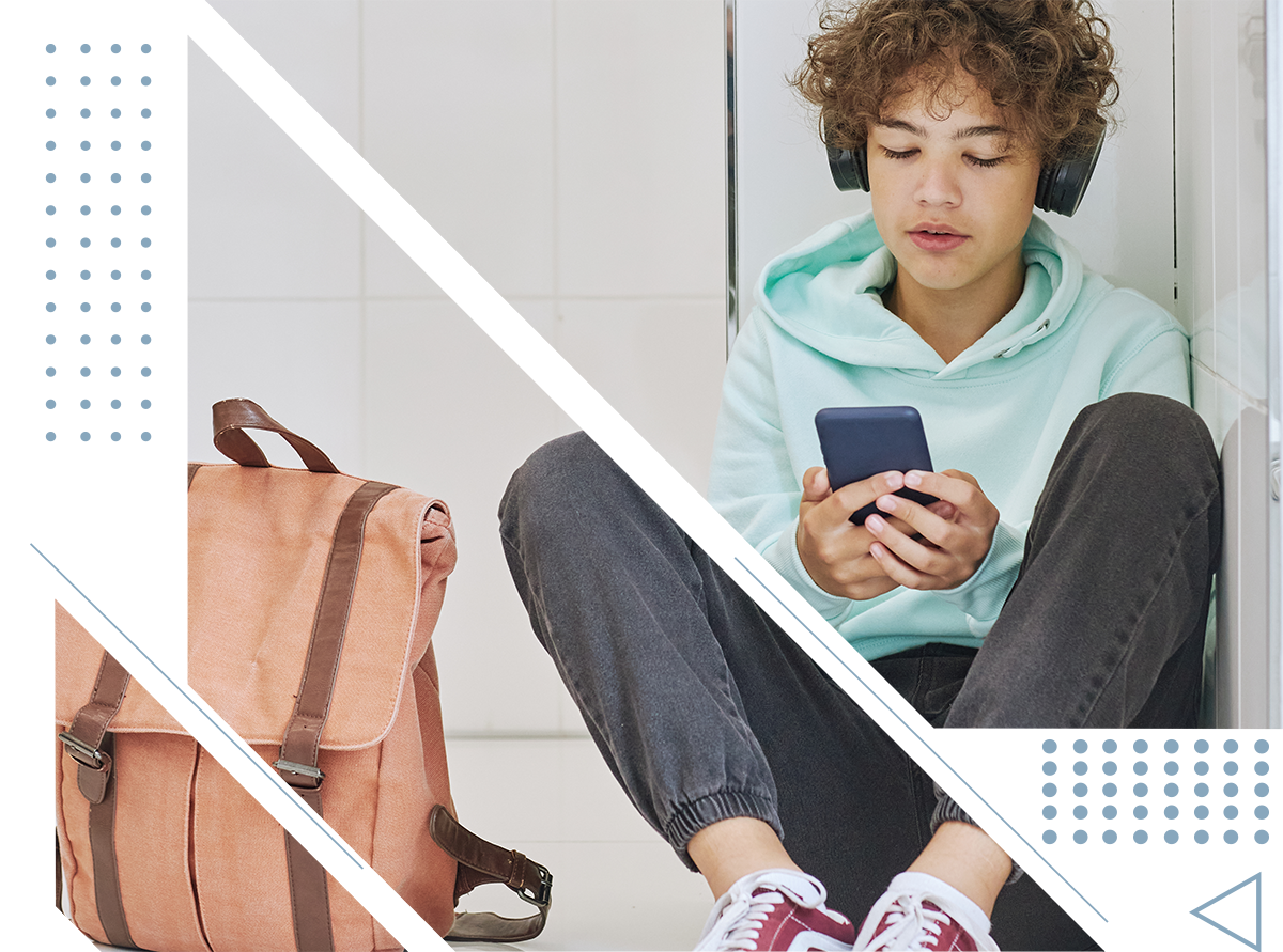 A young boy is sitting on the floor looking at his cell phone.