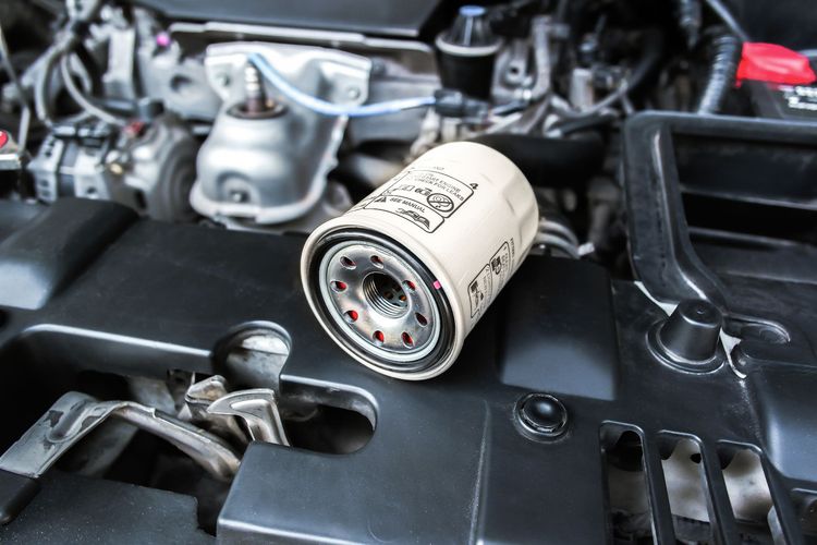 Vano motore dell'auto con un filtro dell'olio bianco appoggiato sopra il coperchio nero del motore.