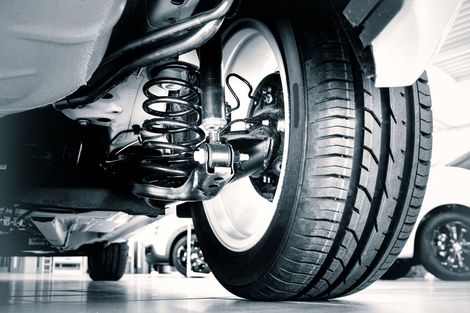 Primo piano di una ruota e del sistema di sospensione di un'auto in un garage, che mostra i dettagli del battistrada e della molla.