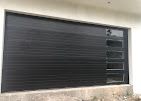 A black garage door is sitting on top of a white wall next to a window.