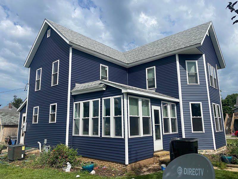 Blue two-story house with white trim and a screened porch under a cloudy sky