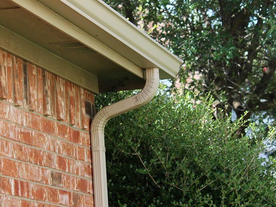 A close up of a gutter on the side of a brick house.