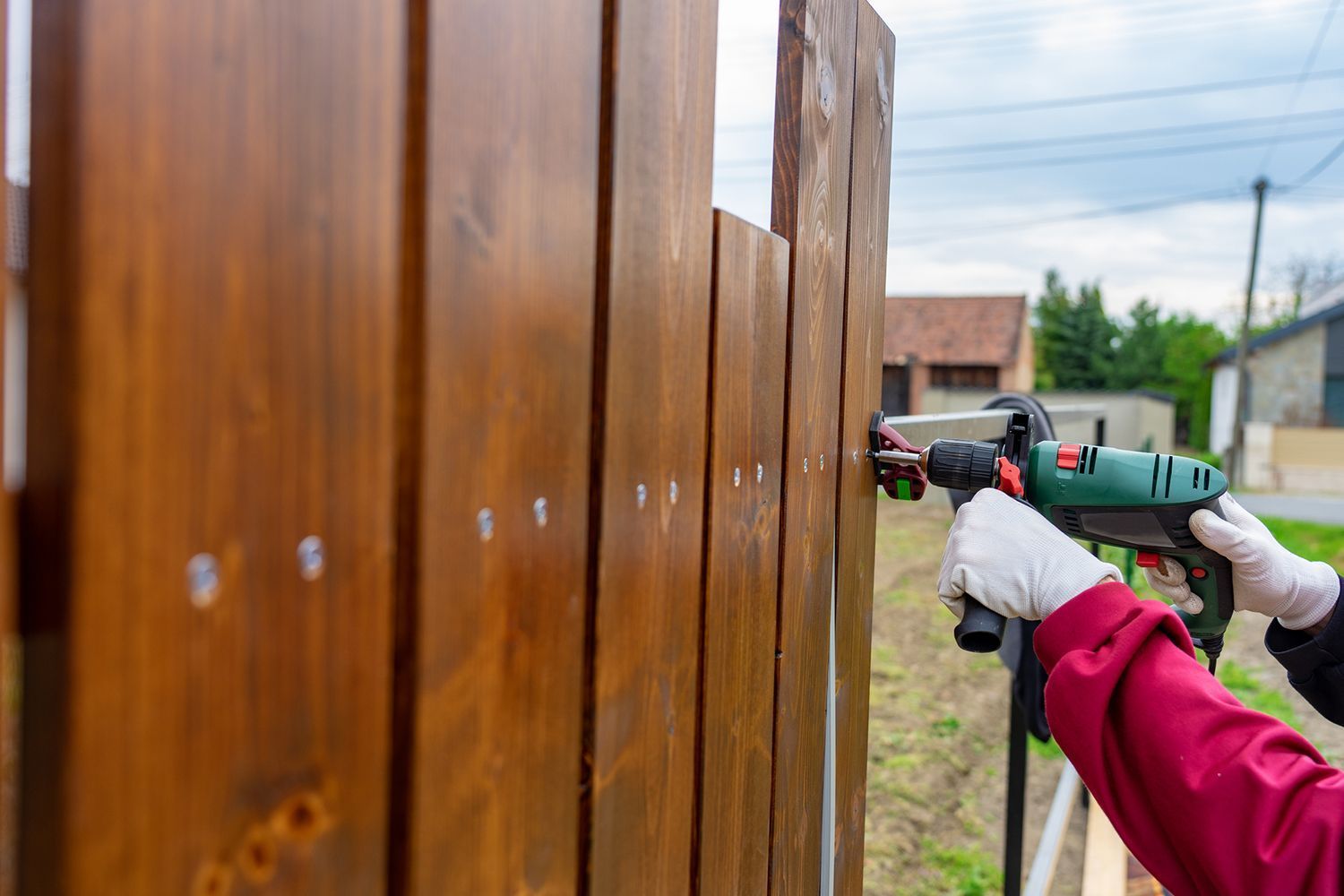 People installing a wooden fence with a cordless drill outdoors