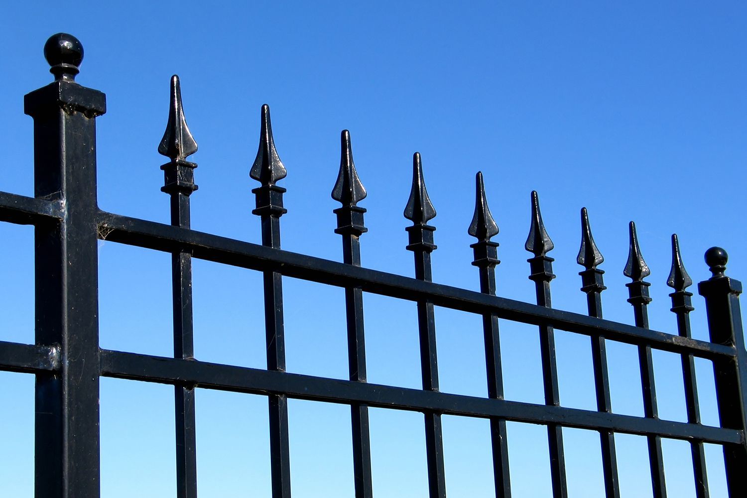 Black wrought-iron fence with pointed finials against a blue sky