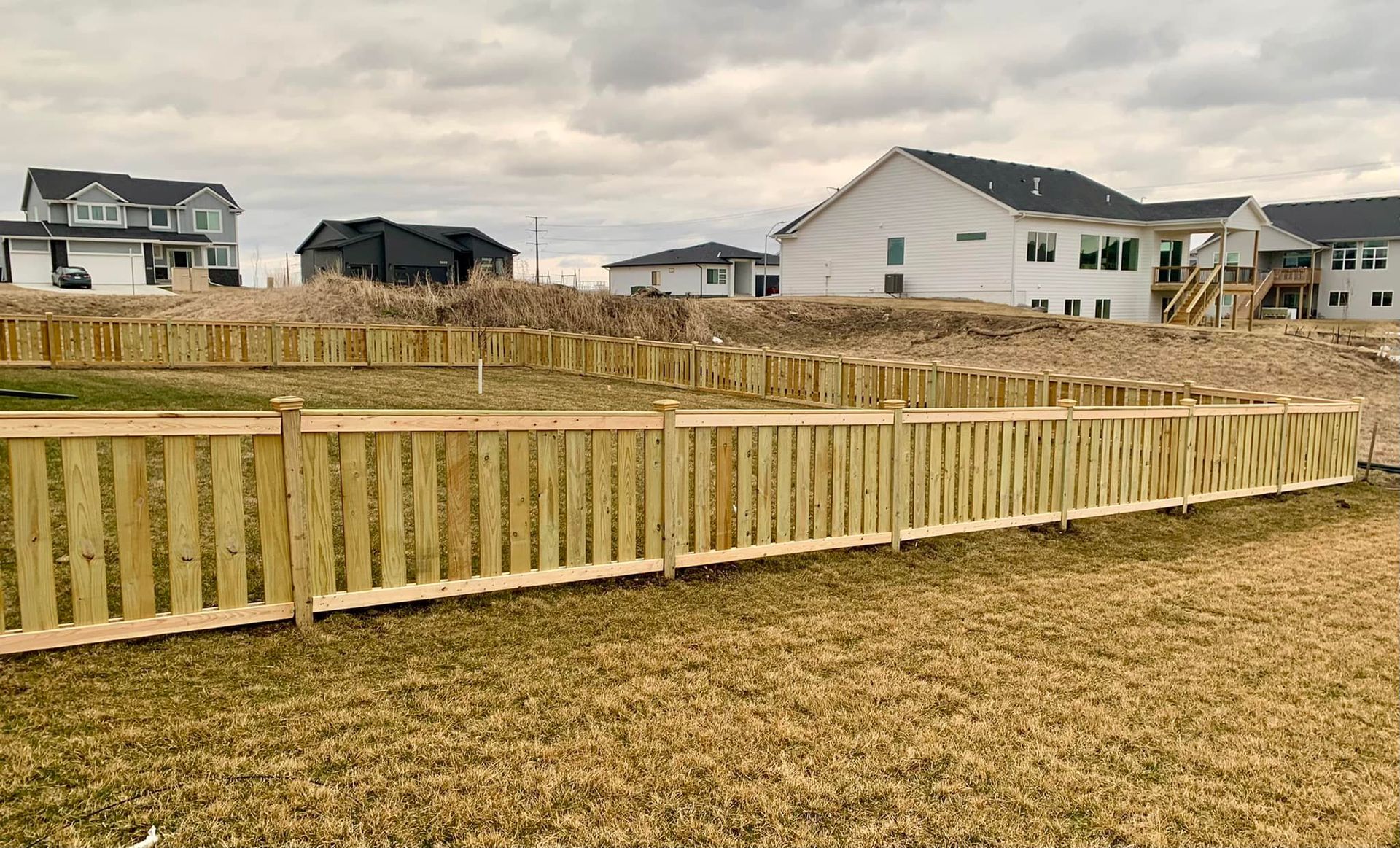 Wooden fence enclosing a muddy backyard in a suburban neighborhood under cloudy skies