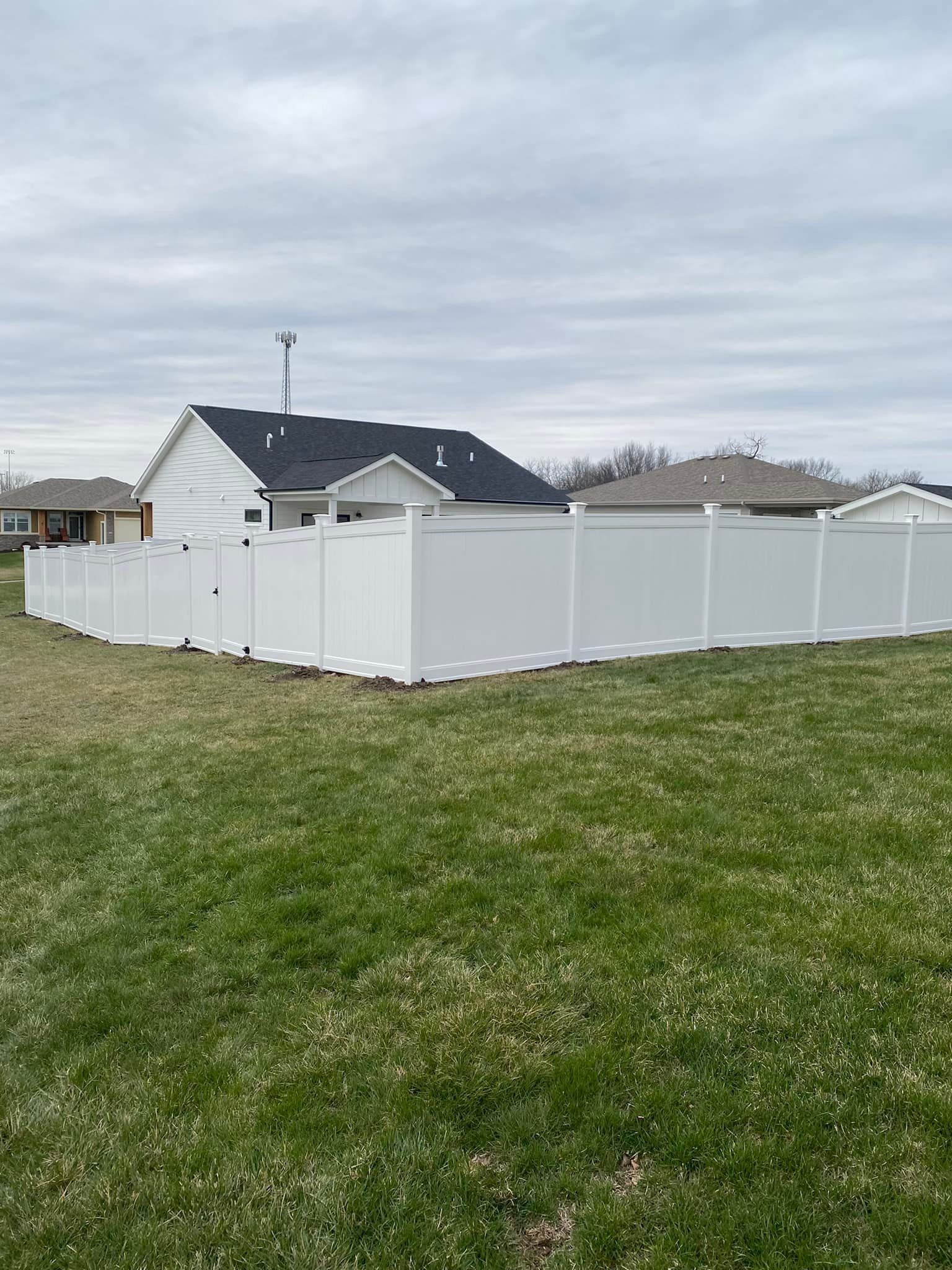 White vinyl fence enclosing a grassy yard beside a dark-roofed house under a cloudy sky