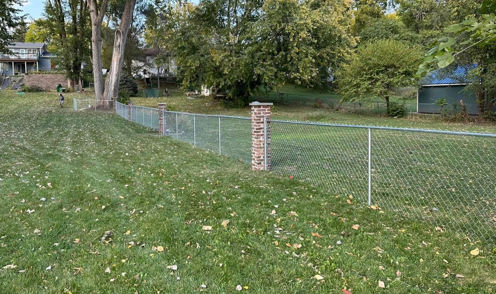 Grassy backyard with chain-link fence, brick post, and trees in a suburban yard
