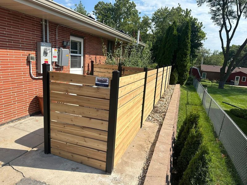 Wooden privacy fence beside a brick house on a narrow side yard by a driveway.
