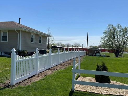 White fence along a grassy yard beside a beige house under a clear blue sky