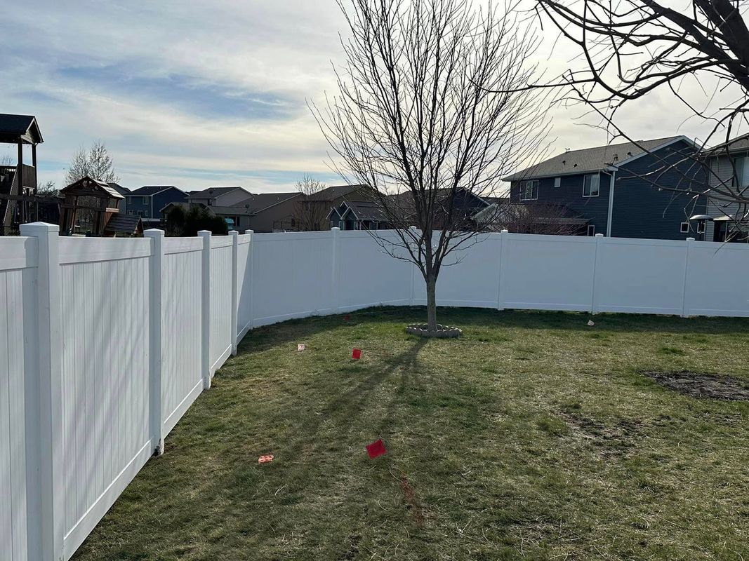 Backyard with white fence, leafless tree, and two red markers on grass under a cloudy sky