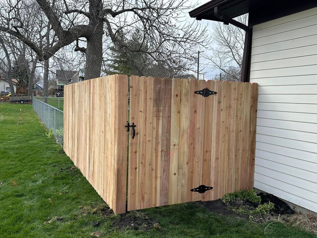 Wooden privacy fence enclosure beside a house, with black hinges and a latch.