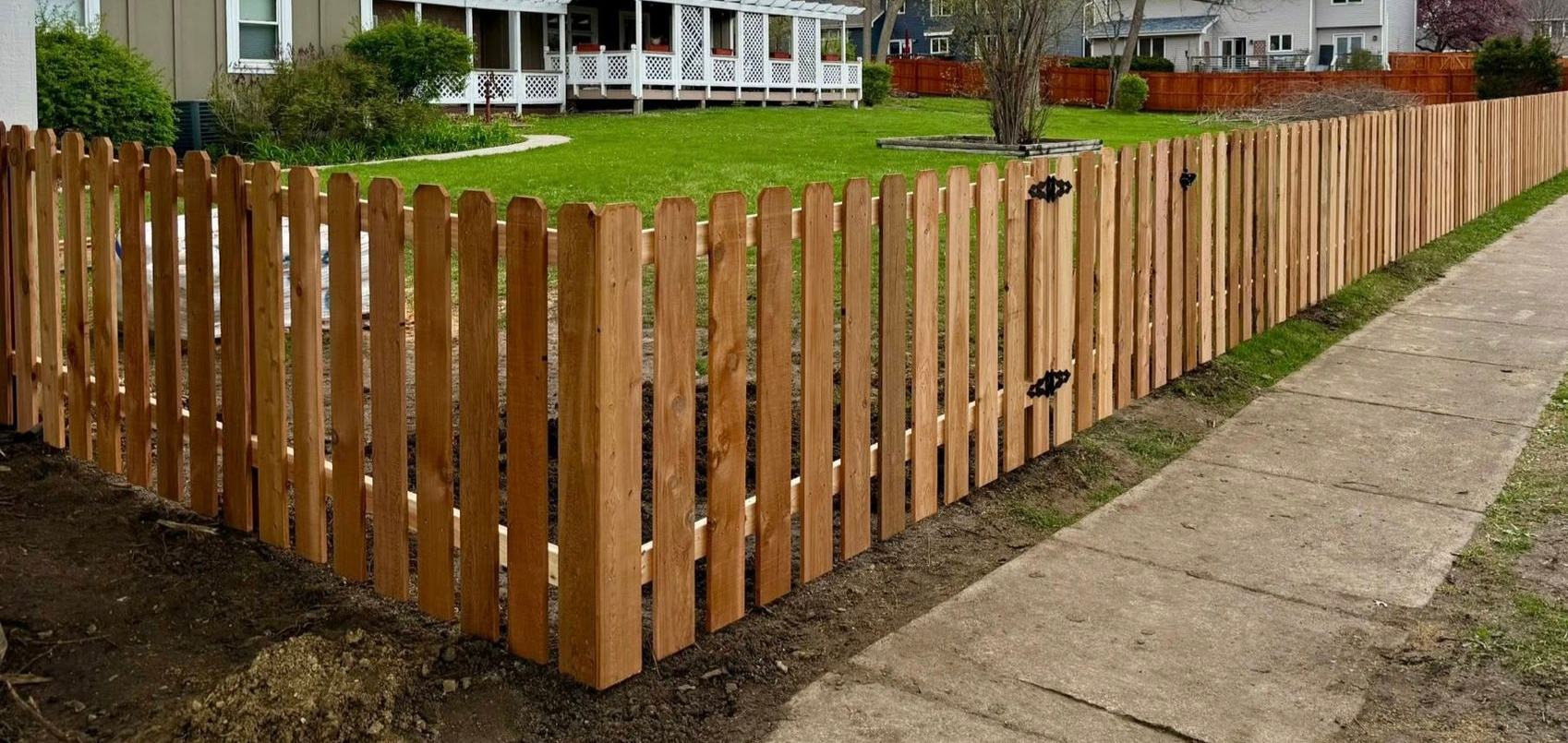 Wooden picket fence lining a yard beside a sidewalk in front of a house