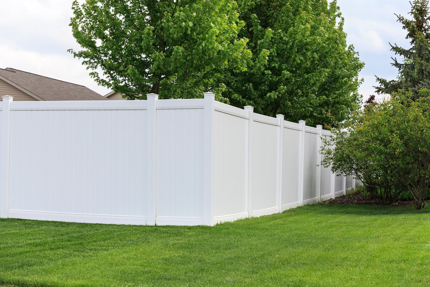 White vinyl privacy fence along a green lawn with trees in the background