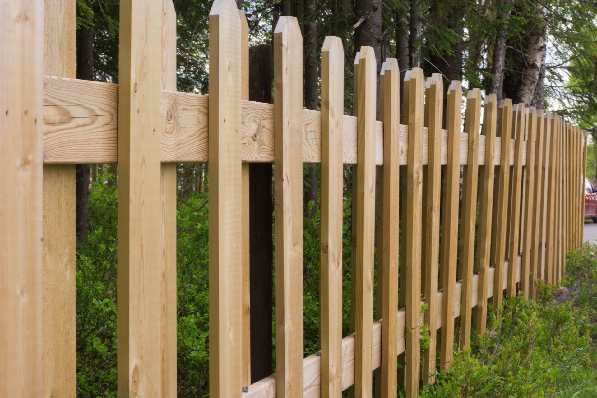 Wooden picket fence along a grassy path with trees in the background
