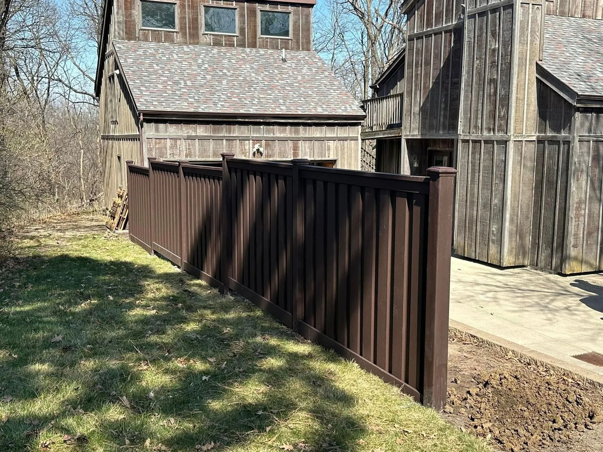 Brown metal fence beside rustic wooden buildings in a grassy yard