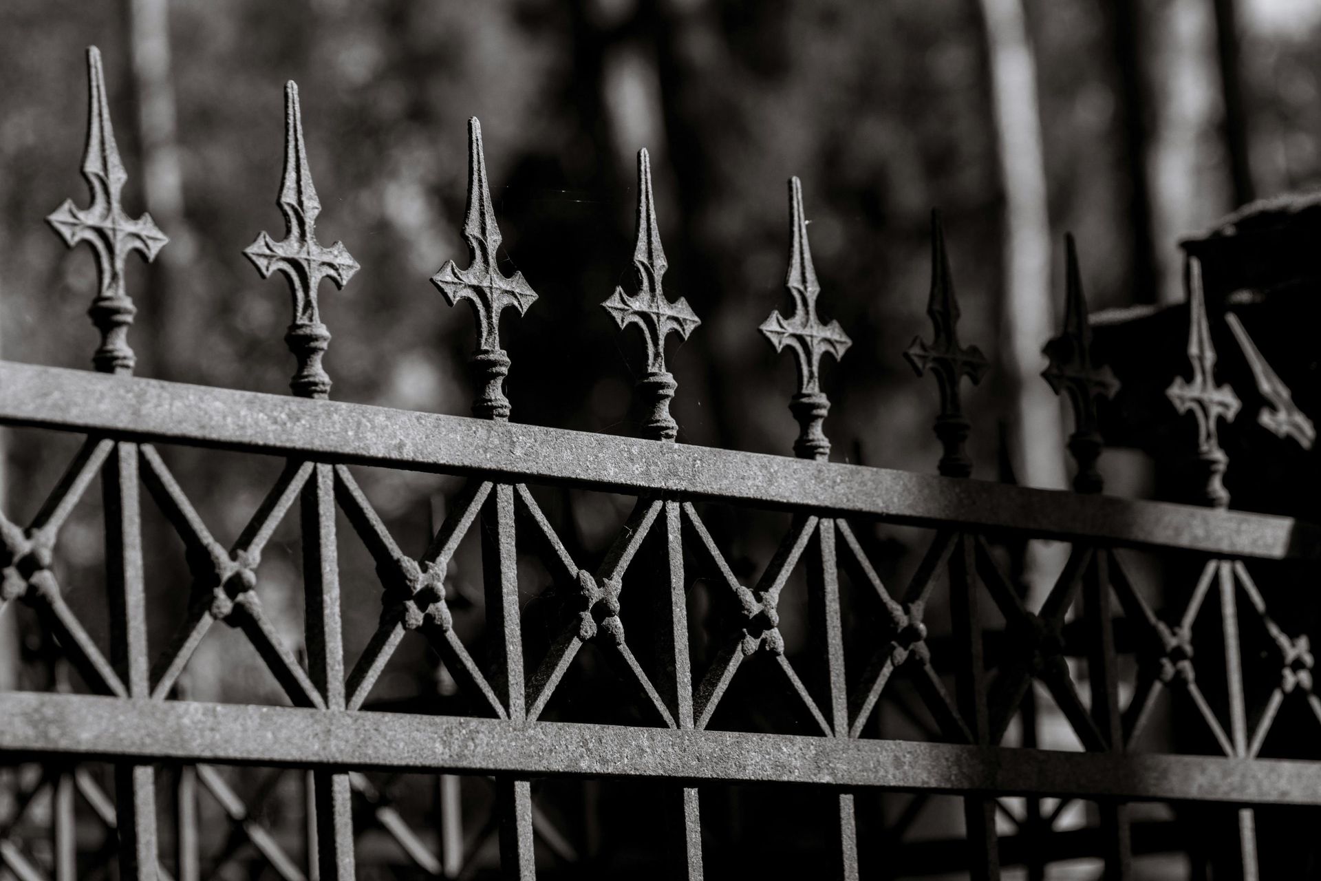 Black wrought-iron fence with decorative spear tops against a blurred dark background