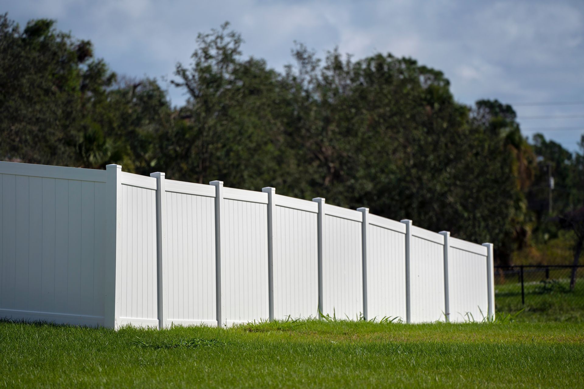 White vinyl fence on a grassy field with trees and cloudy sky in the background