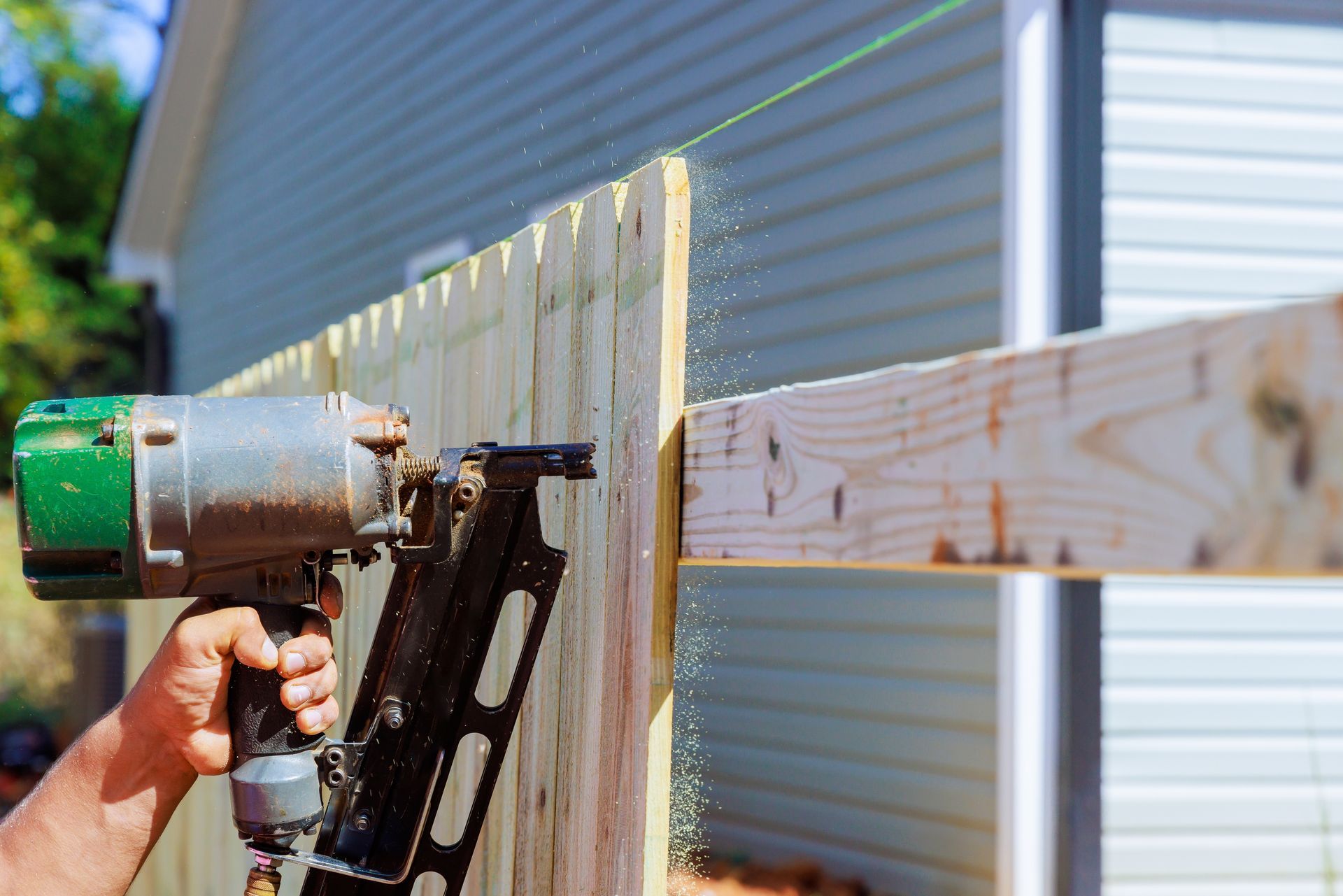 Person using a nail gun to fasten white siding boards to a house exterior