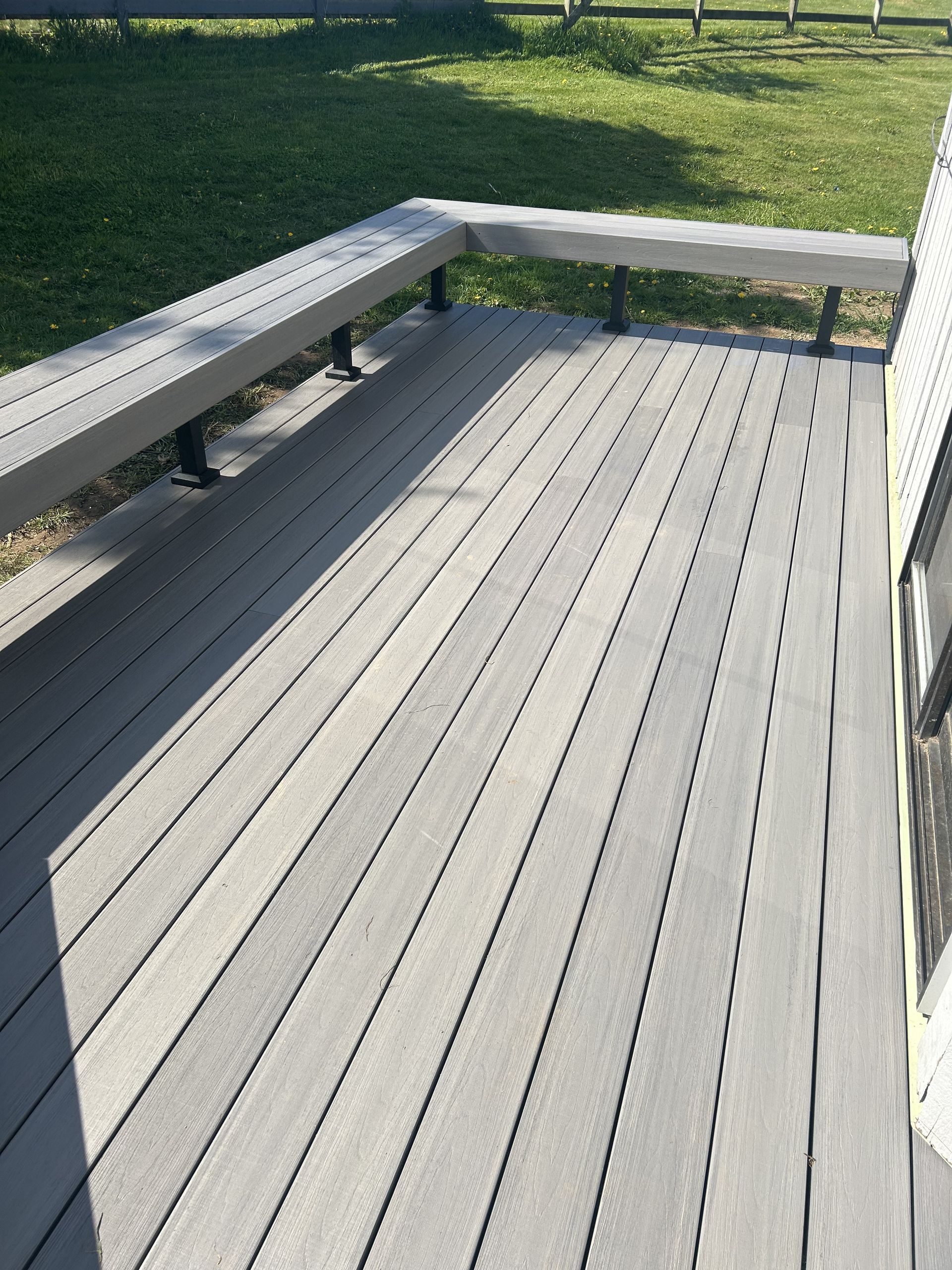 Gray wooden deck with built-in benches beside a grassy yard in sunlight