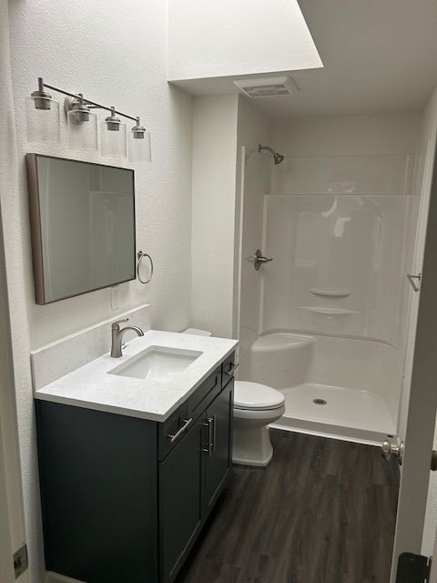 Small modern bathroom with dark vanity, sink, mirror, toilet, and shower stall.