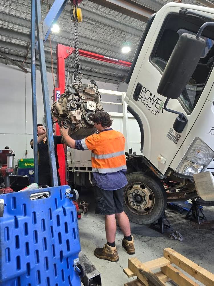 Two Mechanics Removing A Truck Engine Using A Hoist In A Workshop — Diesel Engine Rebuilding Australia in Gold Coast, QLD