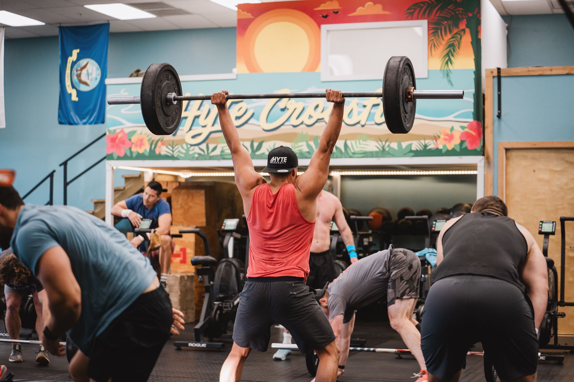 Gym class with people doing synchronized barbell overhead presses in a colorful studio
