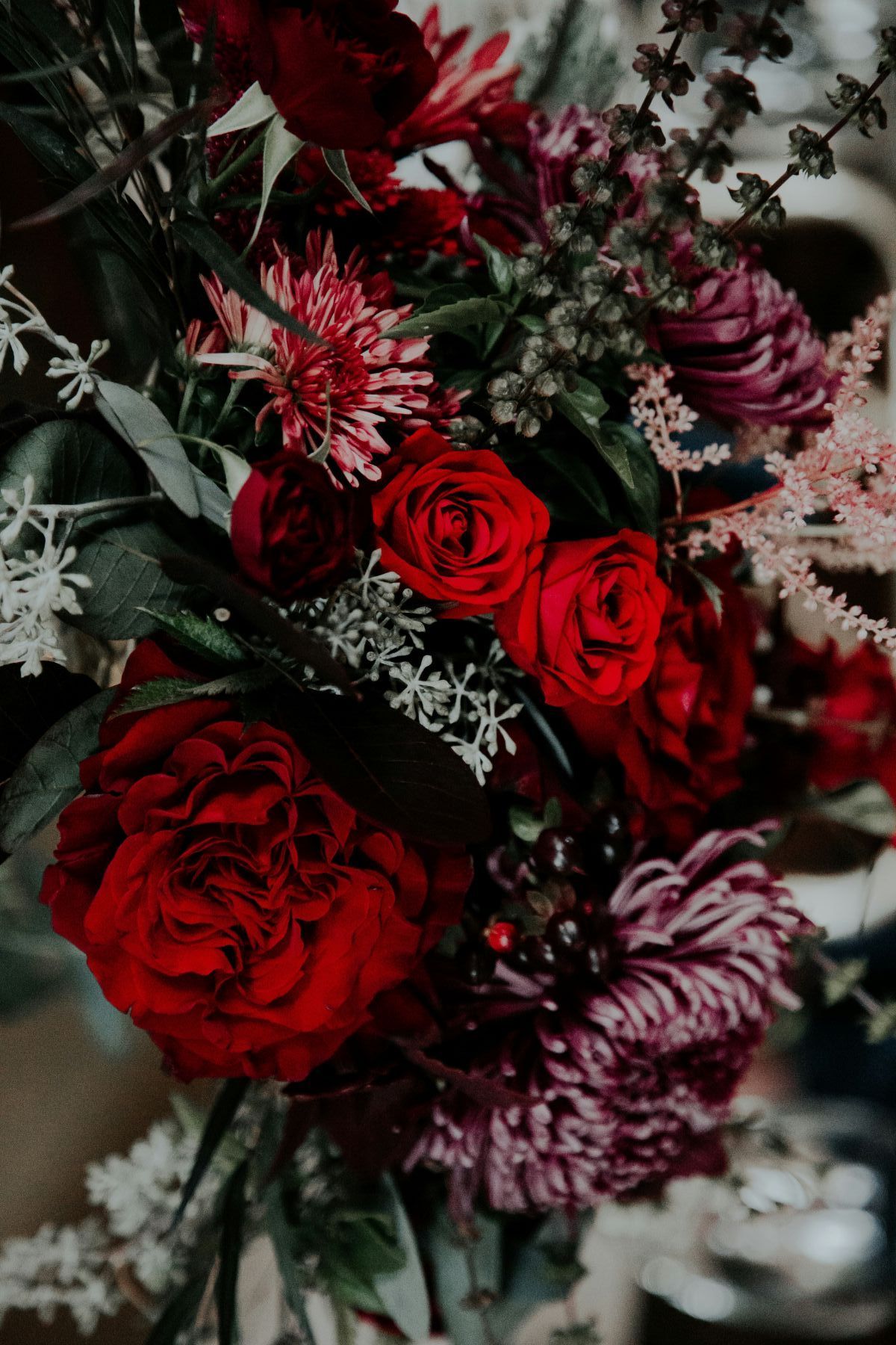 Deep red and burgundy floral arrangement with roses, chrysanthemums, and foliage.