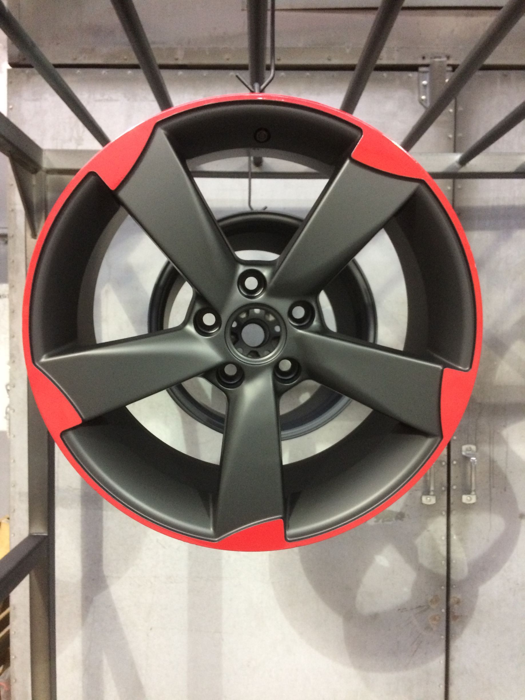 Une roue noire avec une jante rouge est suspendue à un support