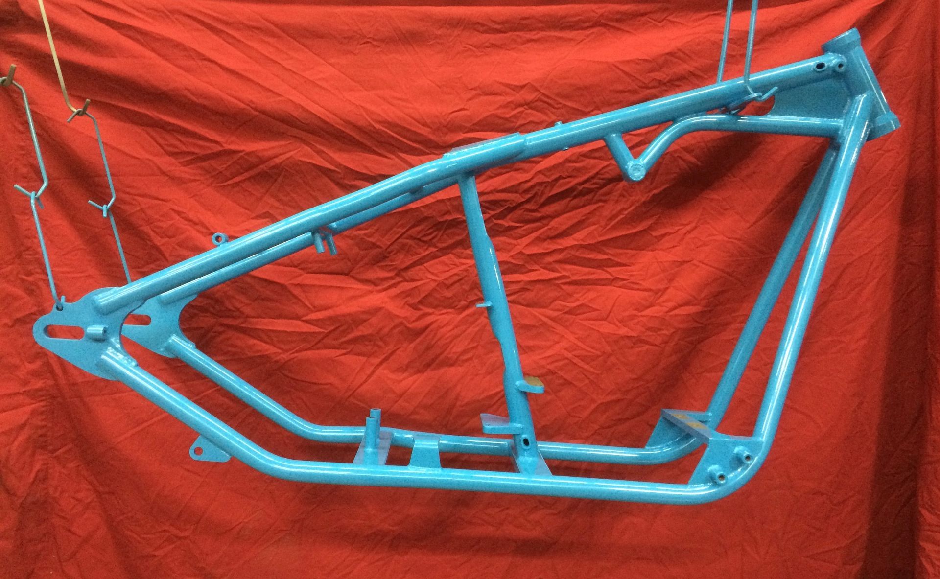 A blue motorcycle frame is hanging on a red cloth