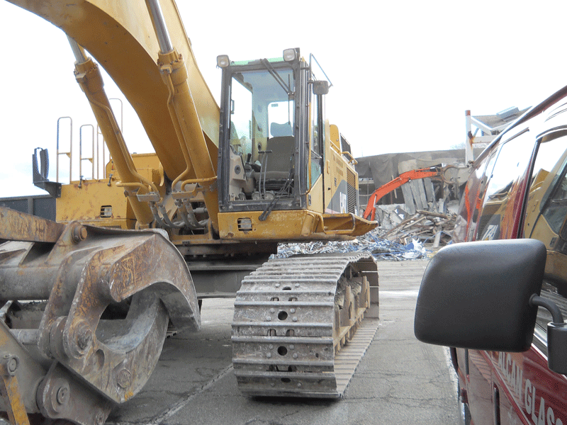 A large yellow excavator is parked next to a red van