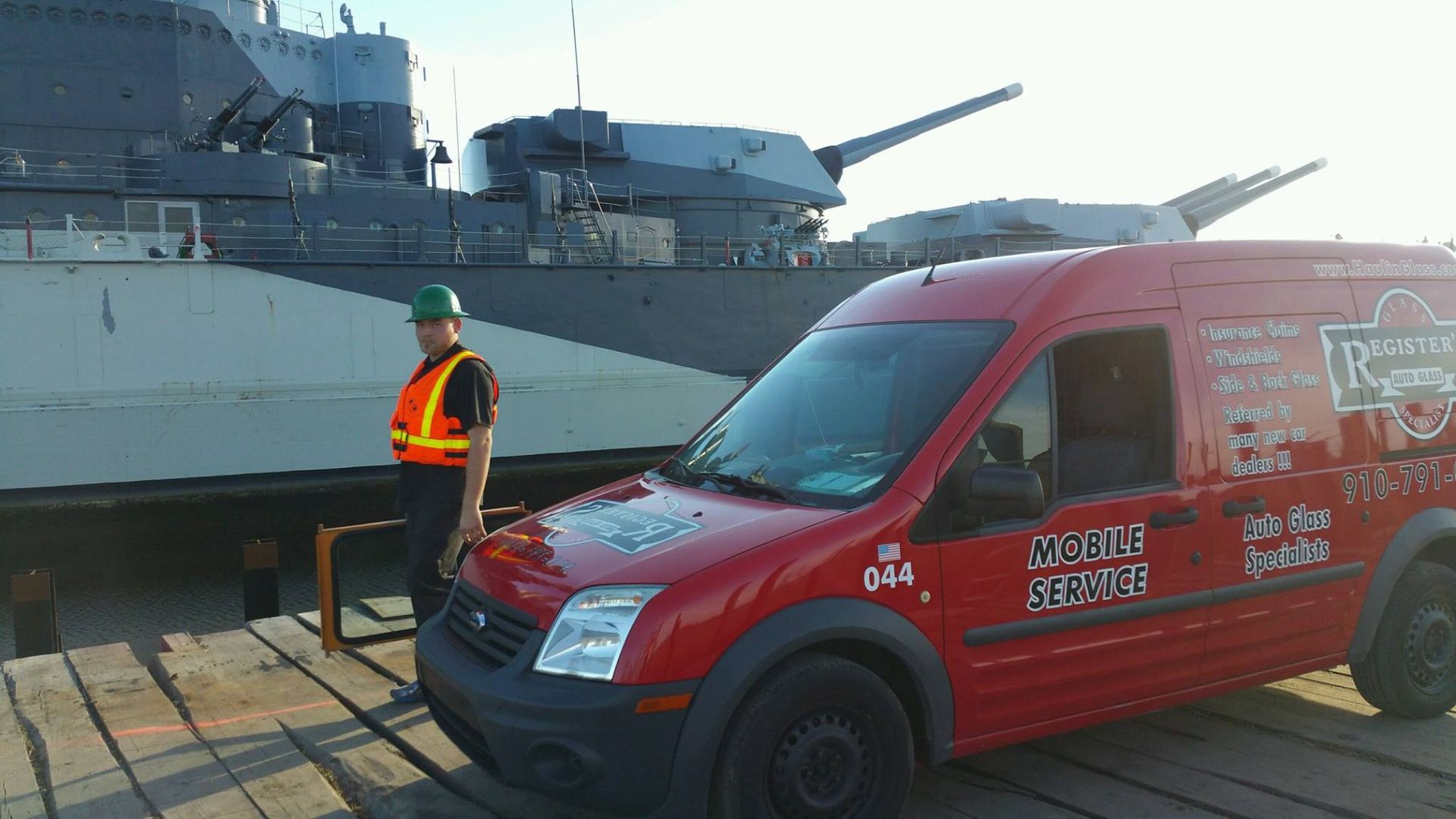 A man is standing next to a red van in front of a large ship