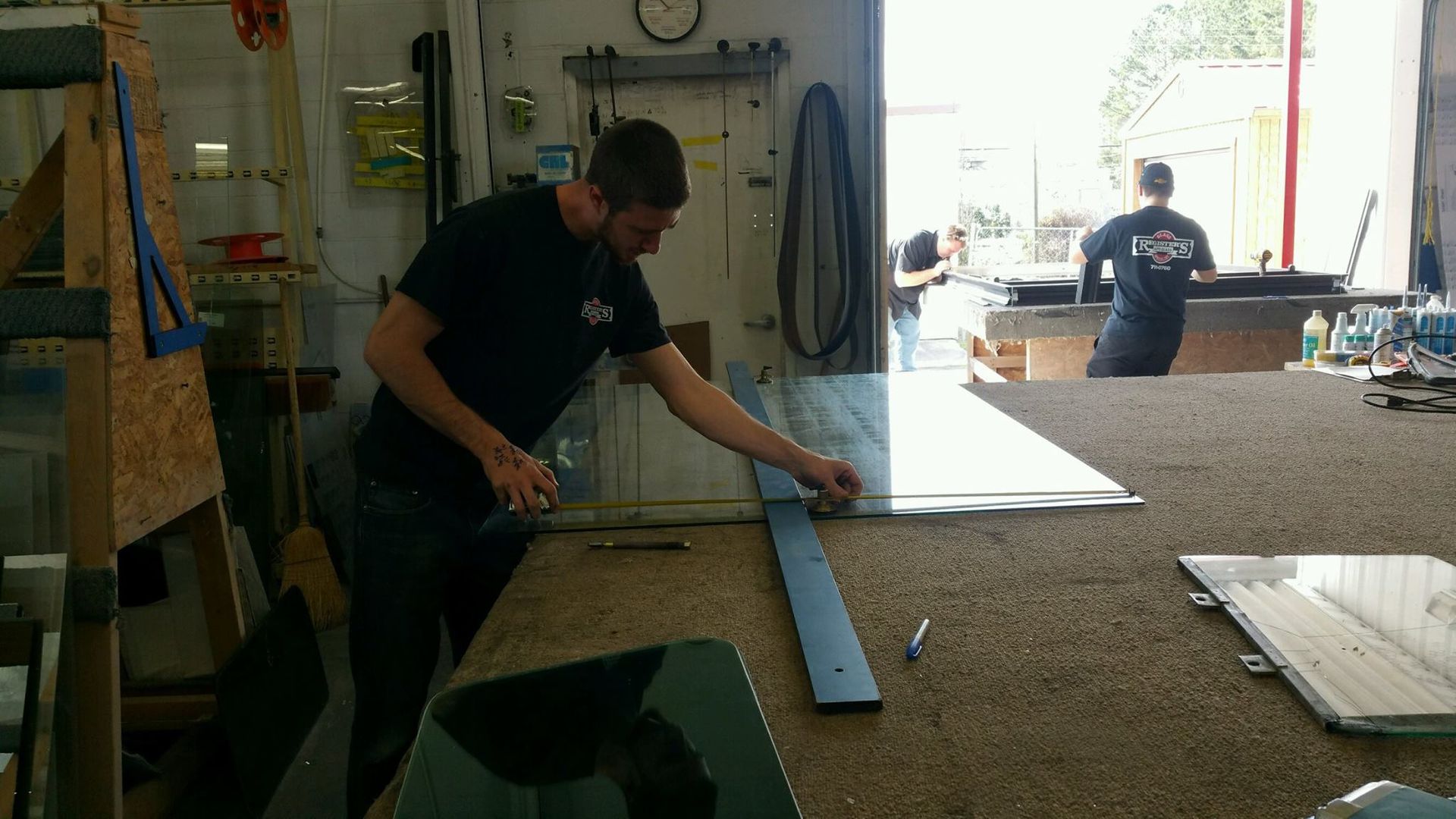 A man is measuring a piece of glass on a table in a workshop
