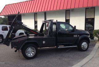 A black tow truck is parked in front of a building with a red roof