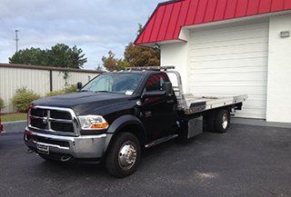 A black tow truck is parked in front of a building with a red roof