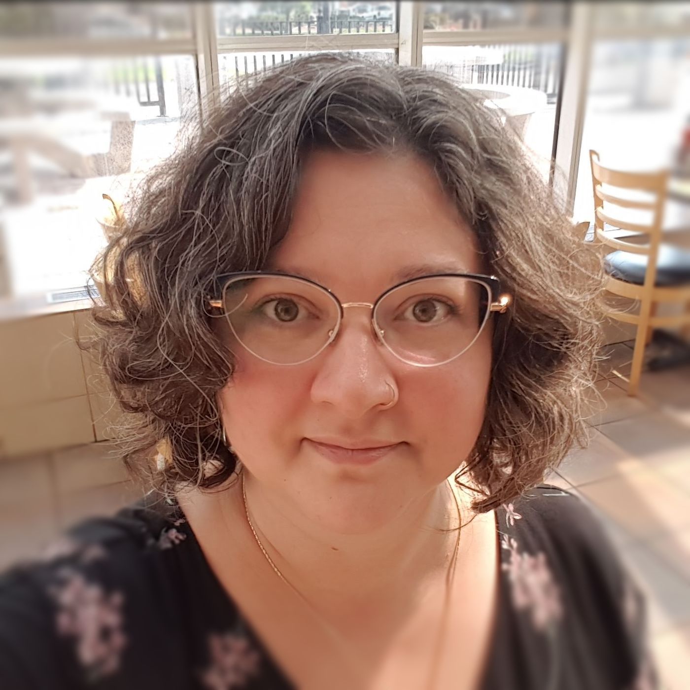 Portrait of a woman with bobbed curly brown hair and glasses.