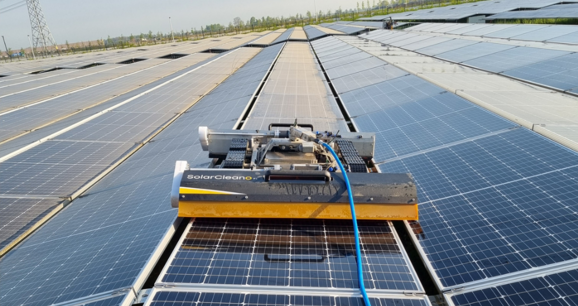 Solar panel cleaning robot moving along rows of blue rooftop solar panels under a clear sky