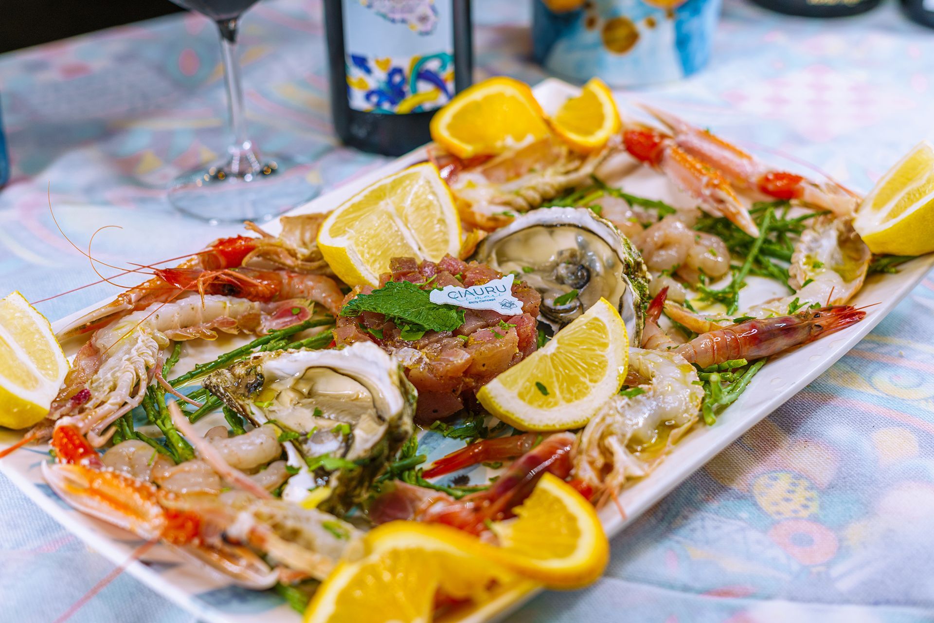 Piatto di frutti di mare con gamberi, ostriche e fette di limone su un tavolo con una bottiglia di vino.