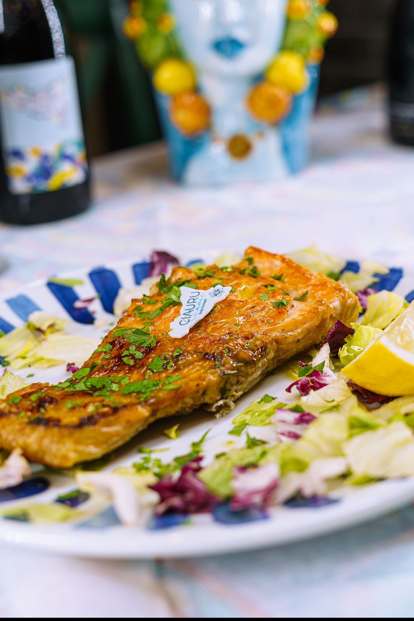 Salmone alla griglia su un piatto con insalata e limone; piatto a strisce blu e bianche.
