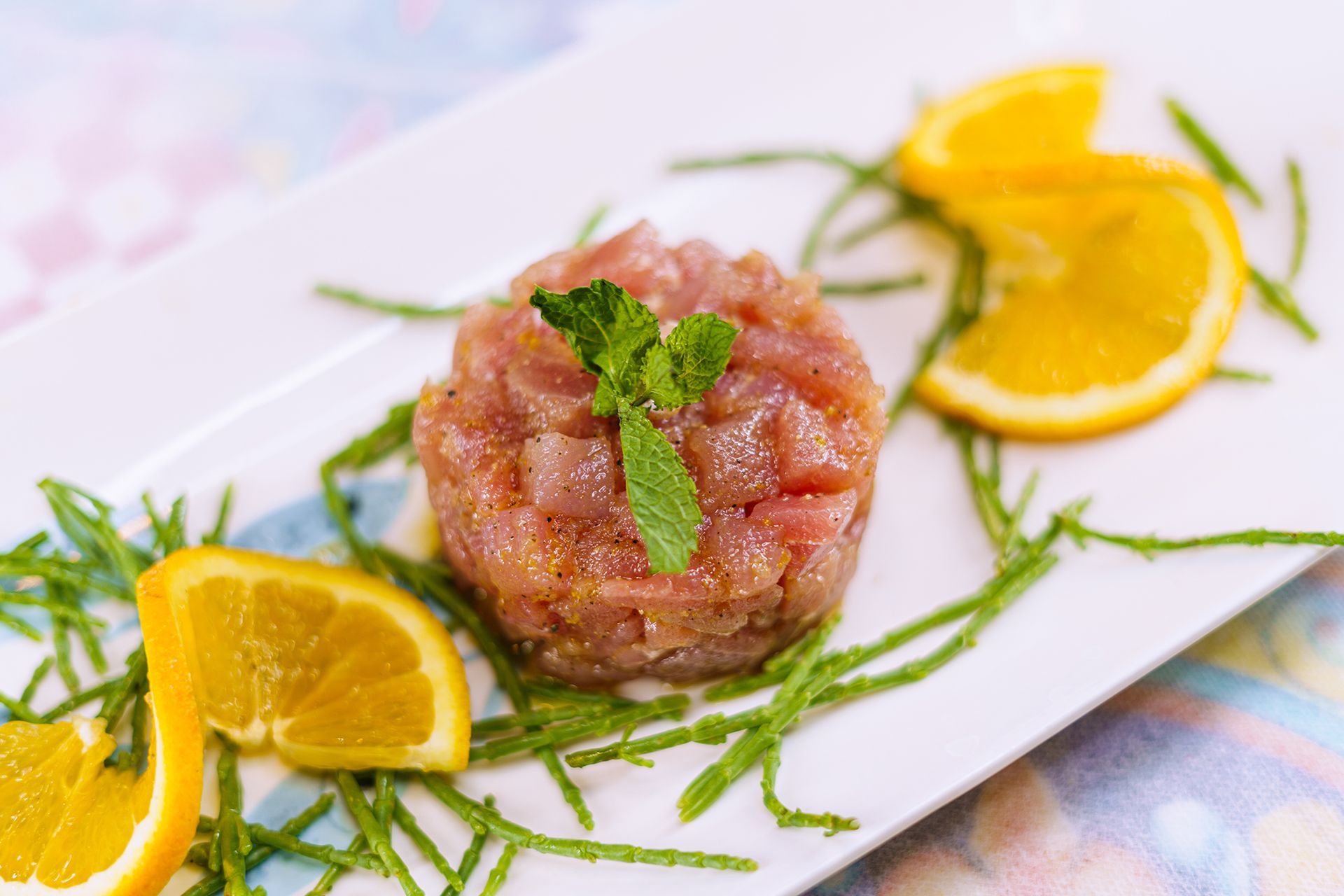 Tartare di tonno crudo su un piatto bianco, guarnita con fette d'arancia e verde.